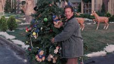 a man standing next to a christmas tree in front of a house with stuffed animals on it