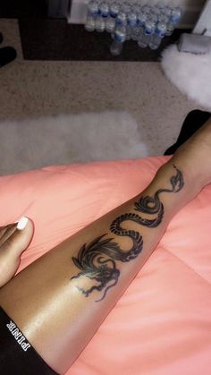 a woman with a dragon tattoo on her arm and leg sitting on a pink blanket