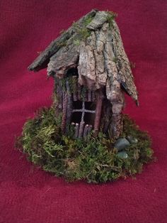 a small house made out of wood and moss on a red cloth covered tablecloth