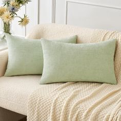 two green pillows sitting on top of a couch next to a vase filled with flowers