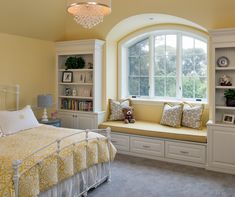 a bedroom with yellow walls, white furniture and a window seat in the corner between two windows