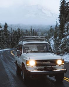 a white toyota pickup truck driving down a road in the snow with mountains in the background