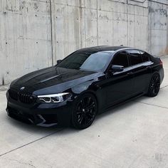 a black bmw is parked in front of a concrete wall with no people around it