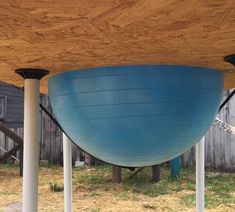 a large blue bowl sitting under a wooden structure on top of grass covered ground next to two white pillars