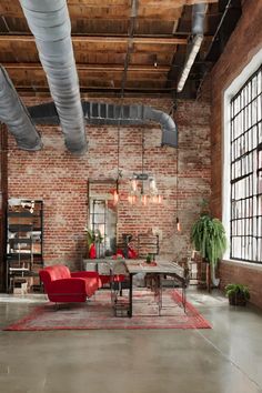 an industrial style living room with exposed brick walls and large windows, red chairs and a rug on the floor