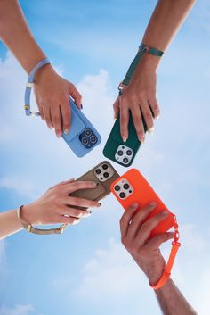 four people holding cell phones in the air with their hands on top of each other