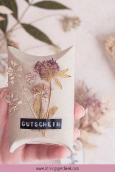 a hand holding a small bag with flowers on it and the words gutschein written in black