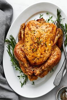 a whole chicken on a white plate with herbs