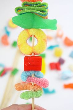 a hand holding a candy lollipop with donuts on top and rainbow candies around it