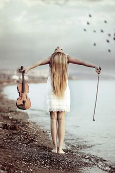 a woman walking on the beach holding a violin and an instrument in her right hand