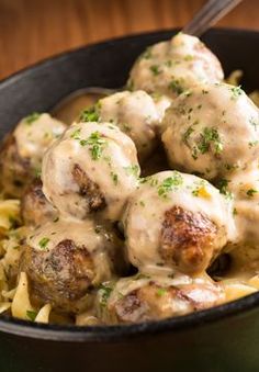 a bowl filled with meatballs covered in gravy and pasta on top of a wooden table