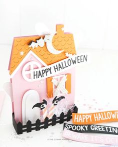 a pink house with halloween decorations on the front and side, sitting next to a sign that says happy halloween