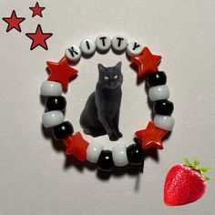 a black cat sitting on top of a red and white beaded necklace next to a strawberry