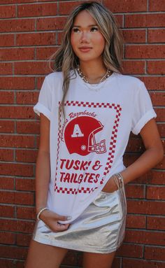 New and improved! One of our favorite designs "Tusks & Tailgates" got an upgrade this year and features a vintage Razorback helmet and trendy checkered frame. Pair with a cute skirt or denim cut offs for an easy gameday look. WE ONLY OFFER STORE CREDIT FOR RETURNS! Feel free to email us at orders@shopriffraff.com or DM us with any questions regarding fit, styling, or our return policy in general. Arkansas Razorbacks Crafts, Arkansas Razorbacks, Denim Cutoffs, Cute Skirts, T Shirt, Clothes, Design