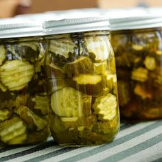 three jars filled with pickles sitting on top of a striped table cloth next to each other