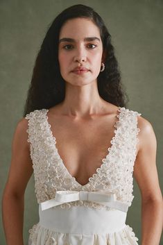 a woman wearing a white dress with flowers on the waist and back, standing in front of a green background