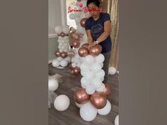 a woman standing next to a bunch of white and rose gold balloons on top of a wooden floor