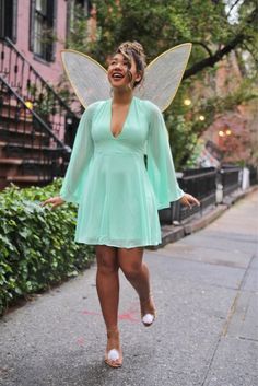 a woman in a green dress is walking down the street with a fairy costume on