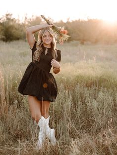 a woman in a black dress and white cowboy boots is posing for a photo with her arms behind her head