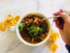 a person is holding a spoon over a bowl of chili and tortilla chips