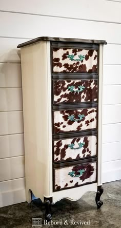 an old dresser is decorated with cow print fabric and black metal handles, as well as drawers