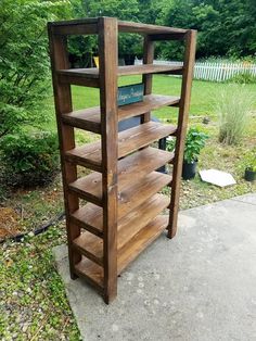 a wooden book shelf sitting on top of a cement slab next to a lush green field