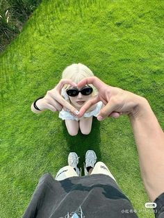 a person sitting in the grass making a heart with their hands