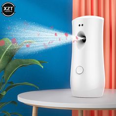 an air freshener dispenser is spraying water on a table next to a potted plant