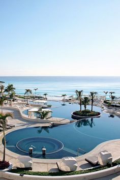 an outdoor swimming pool surrounded by palm trees and the ocean in the backround