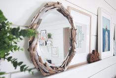 a mirror sitting on top of a mantle next to a potted plant and framed pictures