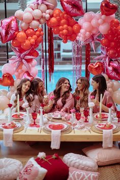 a group of women sitting at a table with pink and red balloons