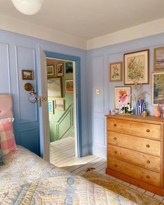 a bedroom with blue walls and pictures on the wall above the bed, along with a chest of drawers