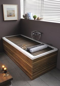 a bath tub with two candles on the side and a window in the back ground