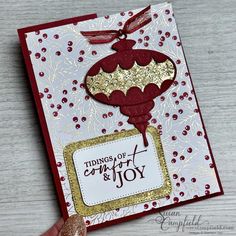 a handmade card with a red and gold ornament hanging from it's side