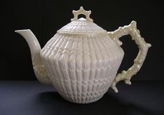 a white ceramic tea pot with a handle and star decoration on the top, sitting on a black surface