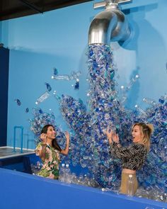 two women standing in front of a blue wall with water pouring from the faucet