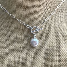 "A freshwater coin pearl is set in a sterling silver bezel and suspended from a sterling silver toggle clasp in this choker.  The smaller links of this sterling silver chain give this necklace a dainty overall look.  It is a good choice for someone not comfortable with the boldness of large size paperclip chains.  The links of the chain measure approximately 3.3mm x 9mm.    The toggle clasp measures 12mm. The freshwater pearl measures approximately 15mm in diameter. The necklace is available in approximate lengths of 15\" - 20\", including the clasp." Short Silver Necklace, Toggle Clasp Necklace, Silver Necklace Simple, Paperclip Chain Necklace, Sterling Silver Choker, Dainty Choker, Layered Necklaces Silver, Coin Pearls, Silver Choker