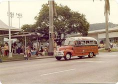 an old red and white bus driving down a street next to a crowd of people