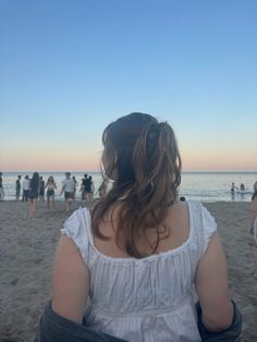 a woman sitting on top of a sandy beach next to the ocean with people in the background