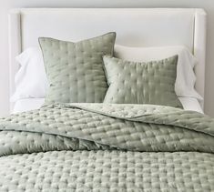 a bed with green comforter and pillows on it's headboard in a bedroom