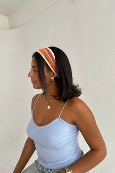 a woman wearing a blue tank top with a striped headband on her head, standing in front of a white wall