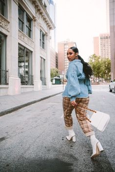 a woman is walking down the street carrying a white bag and wearing plaid pants with high heels