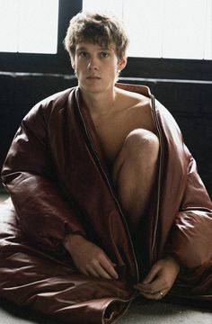 a shirtless man sitting on the floor with his legs wrapped in a brown blanket