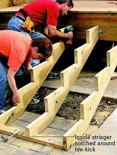 two men are working on some wooden steps outside with tools in their hands and one man is using a power drill