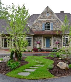 a stone house with green grass and rocks in the front yard, along with landscaping