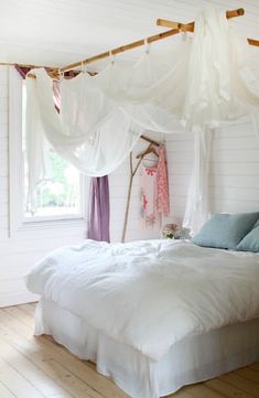 a white bed sitting in a bedroom next to a window with drapes on it