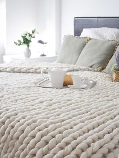 a white bed topped with lots of pillows next to a basket filled with fruit and coffee