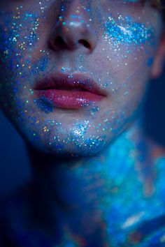 a woman with glitter on her face and body is looking at the camera while she's covered in blue powder