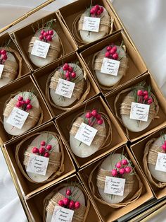 twelve small round cakes with pink flowers in a box on a white cloth covered table