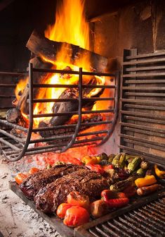 steaks and vegetables being cooked on the grill in front of an open fire pit